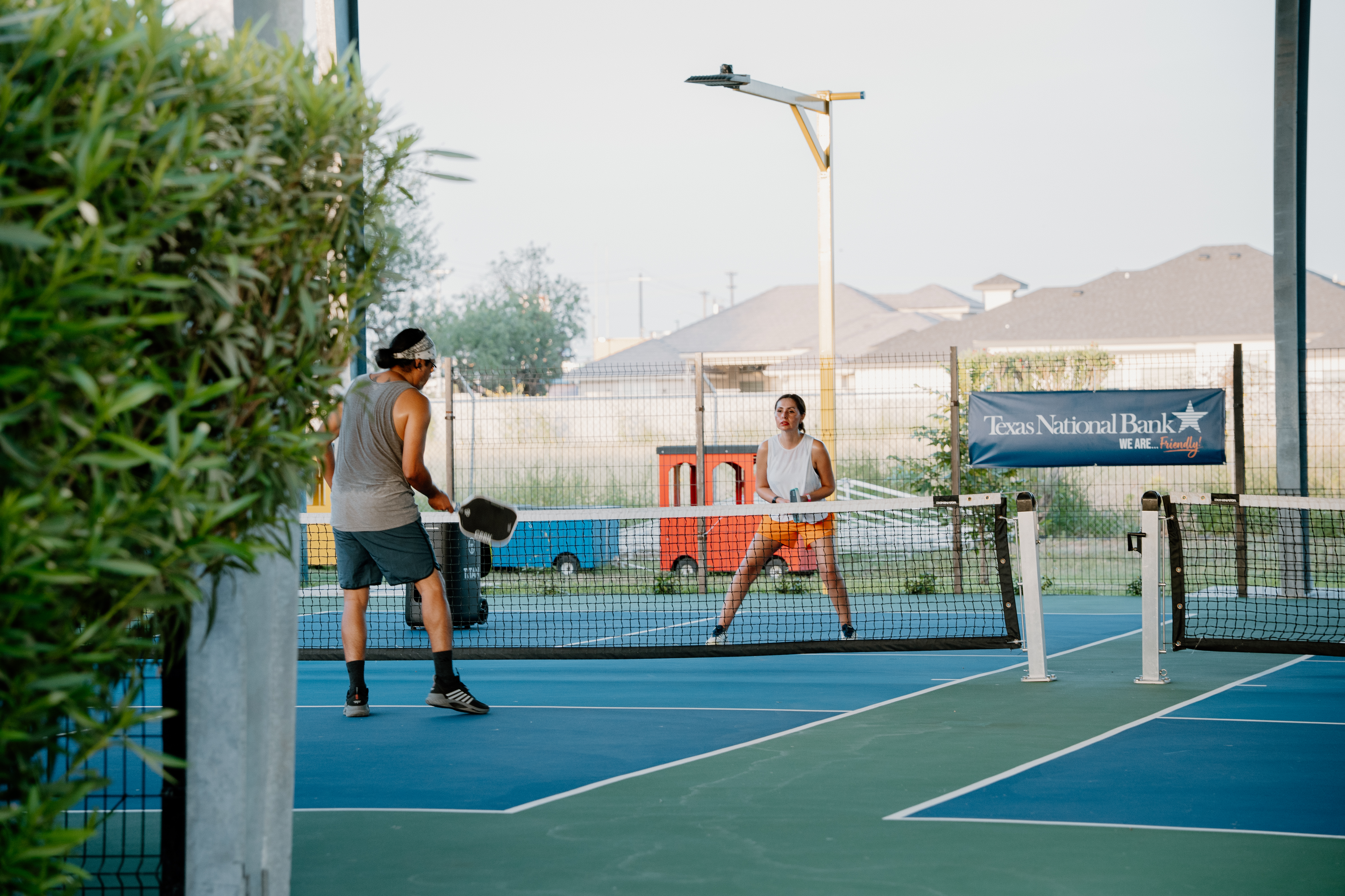 Wide-angle shot of
outdoor pickleball courts at sunset, players mid-rally, vibrant lines and nets
